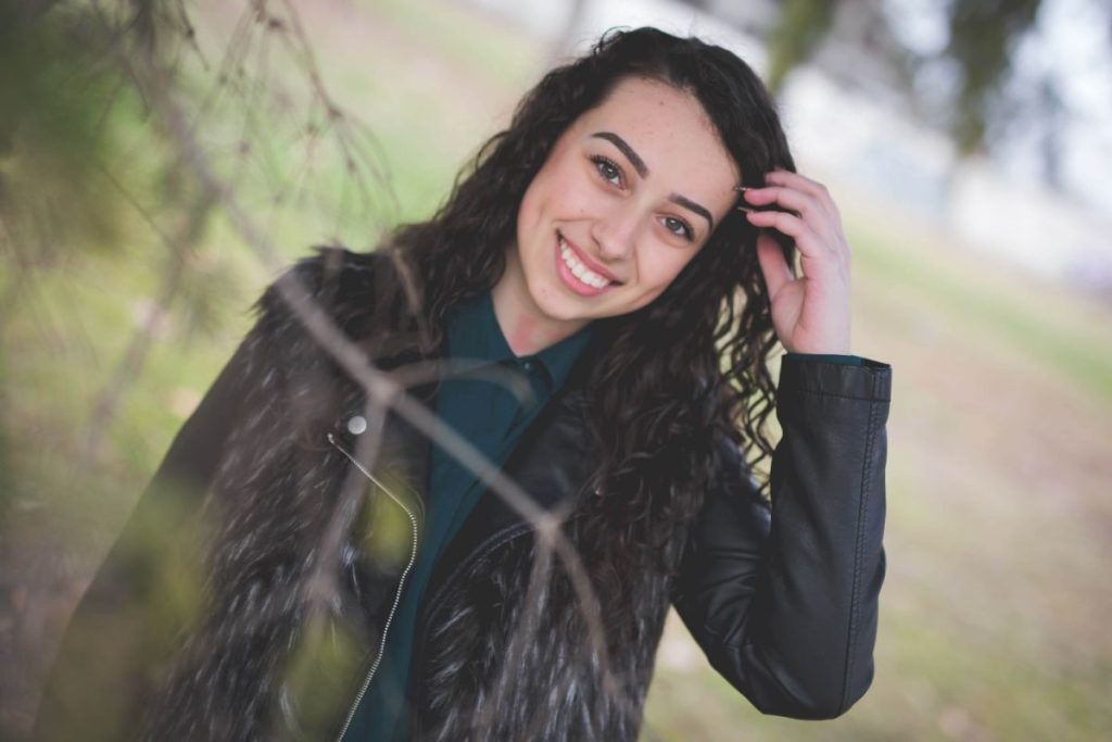 A beautiful curly Bosnian Caucasian woman in a black leather jacket posing outside