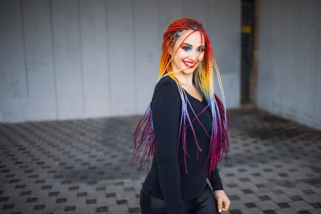 The most beautiful girl in a black elegant dress with bright makeup and multi-colored artificial braids. Beautifully circling and waving long braids against the backdrop of an old building.