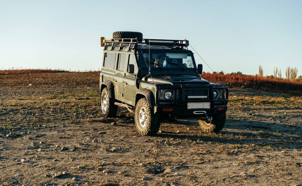 Green massive off-road car parked in empty meadow