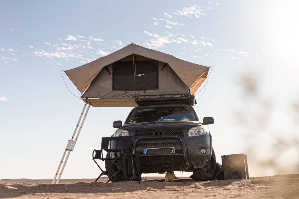 A rooftop tent for camping on the roof rack of an off-road SUV car in a desert