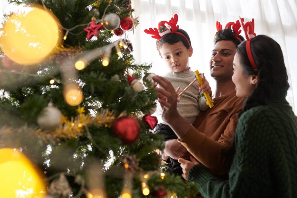 Family with one child wearing reindeer antlers headbands when decorating Christmas tree with toys