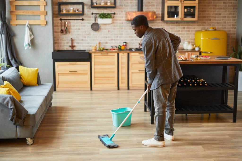 Full length portrait of young African-American man mopping floors while cleaning cozy apartment, copy space