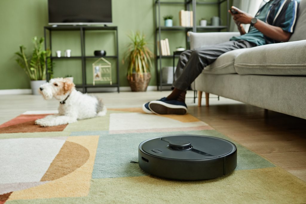 Close up of robot vacuum cleaner on carpet with young man relaxing in background, copy space