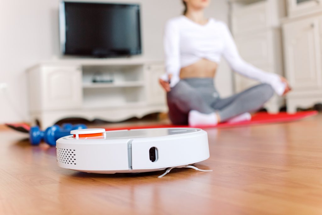Woman sitting in lotus pose doing yoga at home while autonomous vacuum cleaner cleans the floor. Robotic vacuum cleaner cleaning the room while woman relaxing