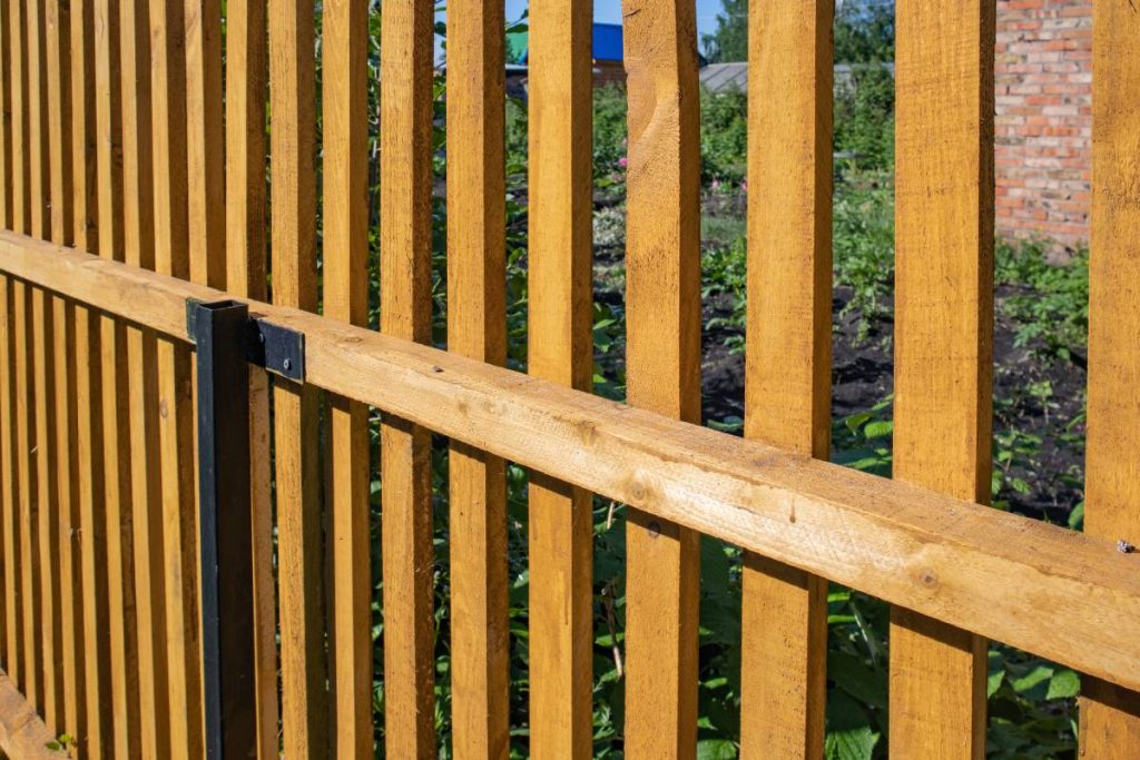 Close-up of a new wooden picket fence in the backyard of a country house, a sunny summer day.