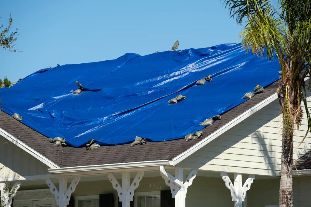 Damaged in hurricane Ian house roof covered with blue protective tarp against rain water leaking until replacement of asphalt shingles.
