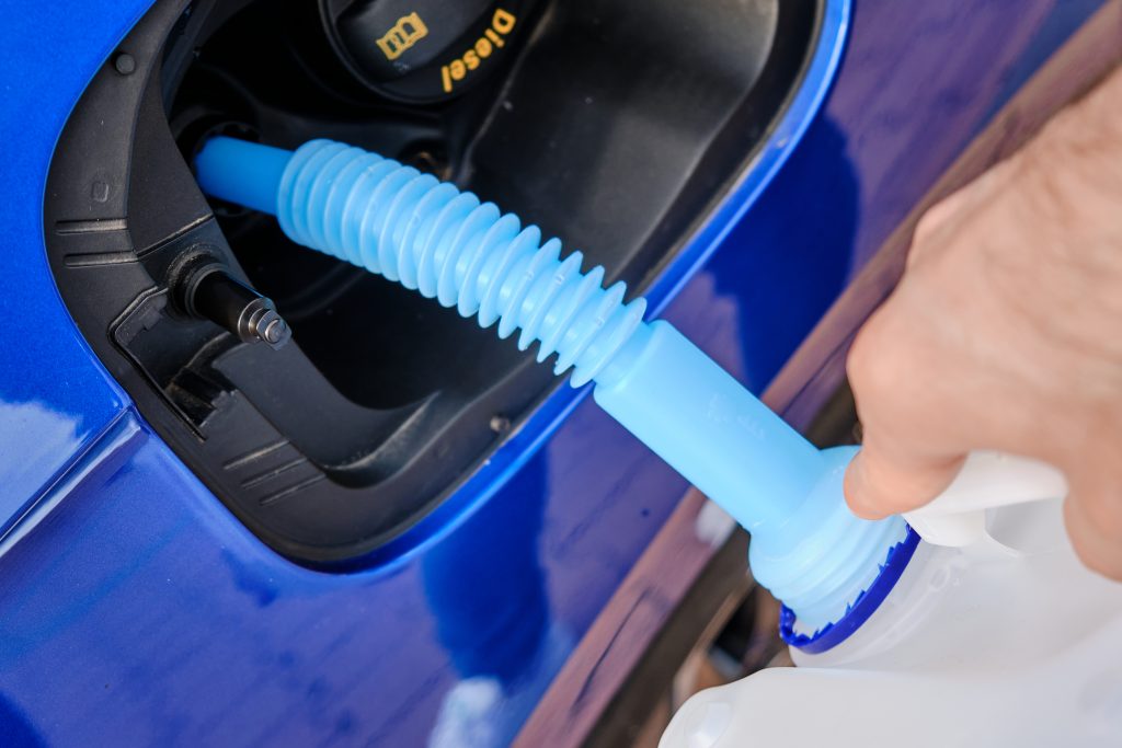 Close up filling of diesel exhaust fluid from canister into the tank of blue car for reduction of air pollution. Environmental or eco friendly solution.