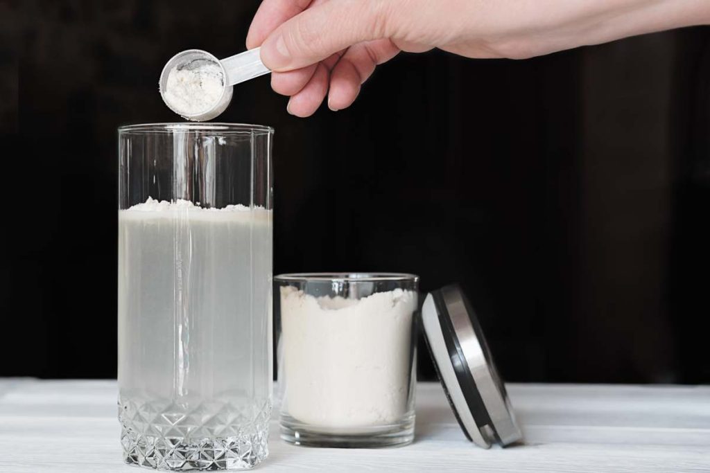 female hand making whey protein drink in a glass and jar with protein powder. supplement for healty joints and beauty. crop view. vegan dietary cocktail