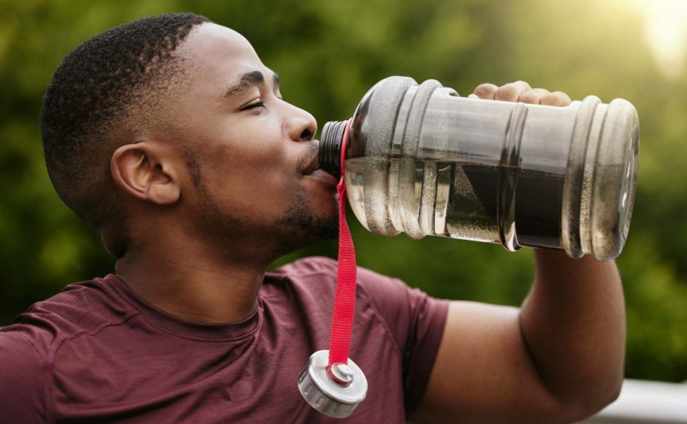 Fitness, nature and man drinking water after a workout in a park for hydration, thirst and rest. Sp.