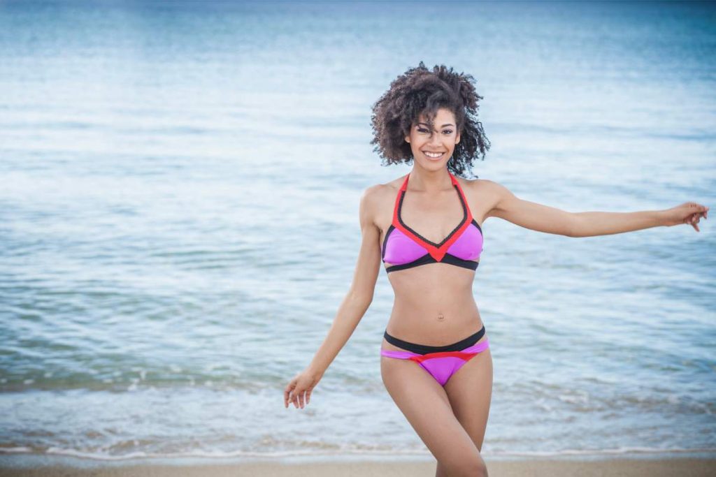 Beautiful young woman wearing pink bikini dancing on beach, Costa Rei, Sardinia, Italy