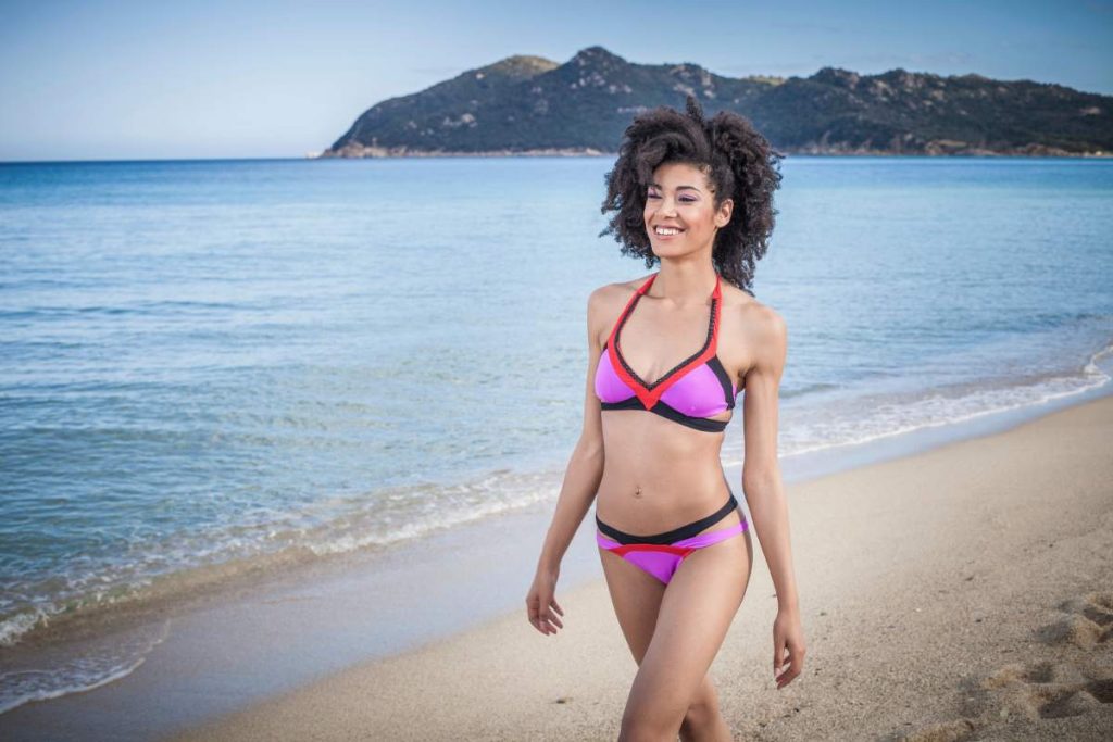 Beautiful young woman wearing pink bikini strolling on beach, Costa Rei, Sardinia, Italy