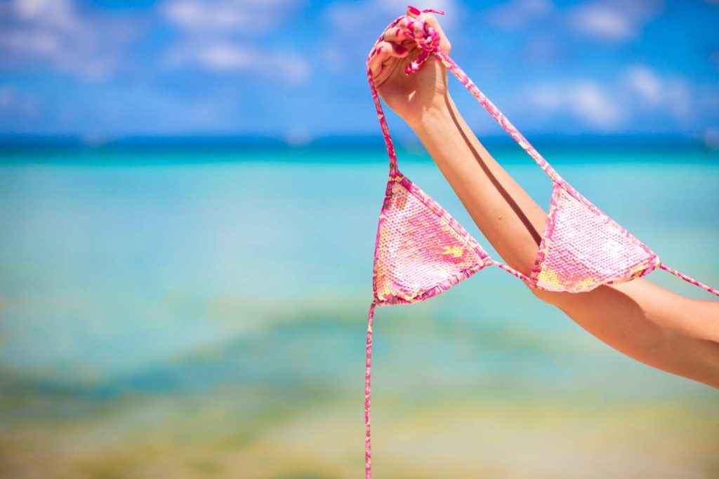 Woman leg holding pink bra isolated on exotic background