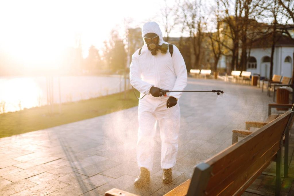 Man wearing protective suit disinfecting public places in the sun with spray chemicals. Covid -19.