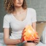 cropped view of curly woman in homewear holding Himalayan salt lamp in bedroom