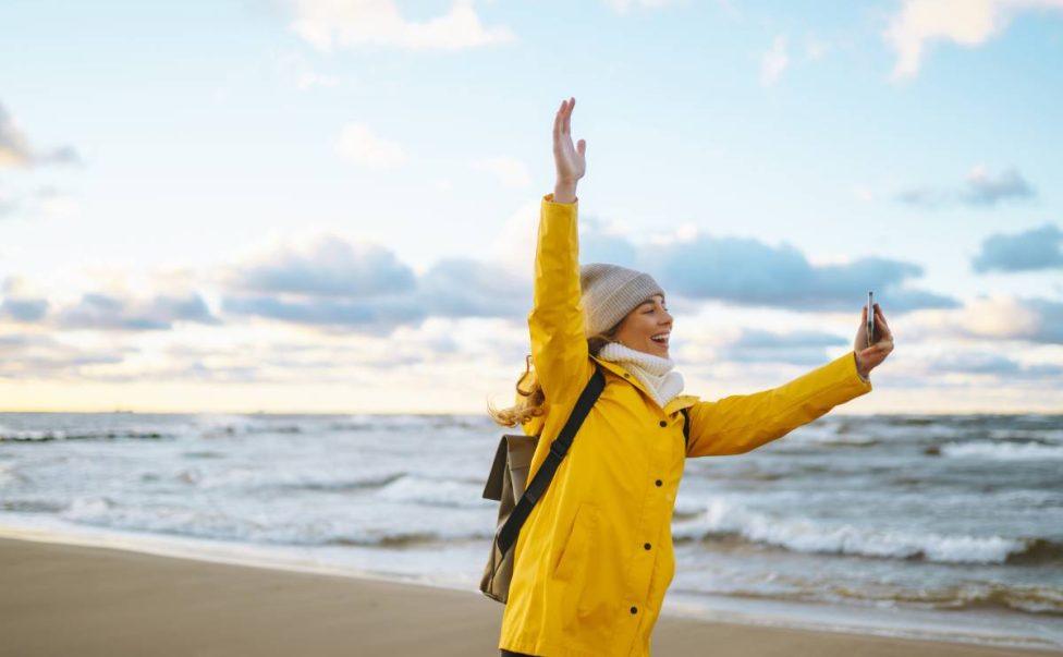 Tourist with phone. Selfie time. Tourist in yellow jacket posing by sea at sunset. Travelling.