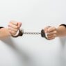 cropped image of girl in handcuffs holding hands through holes on white