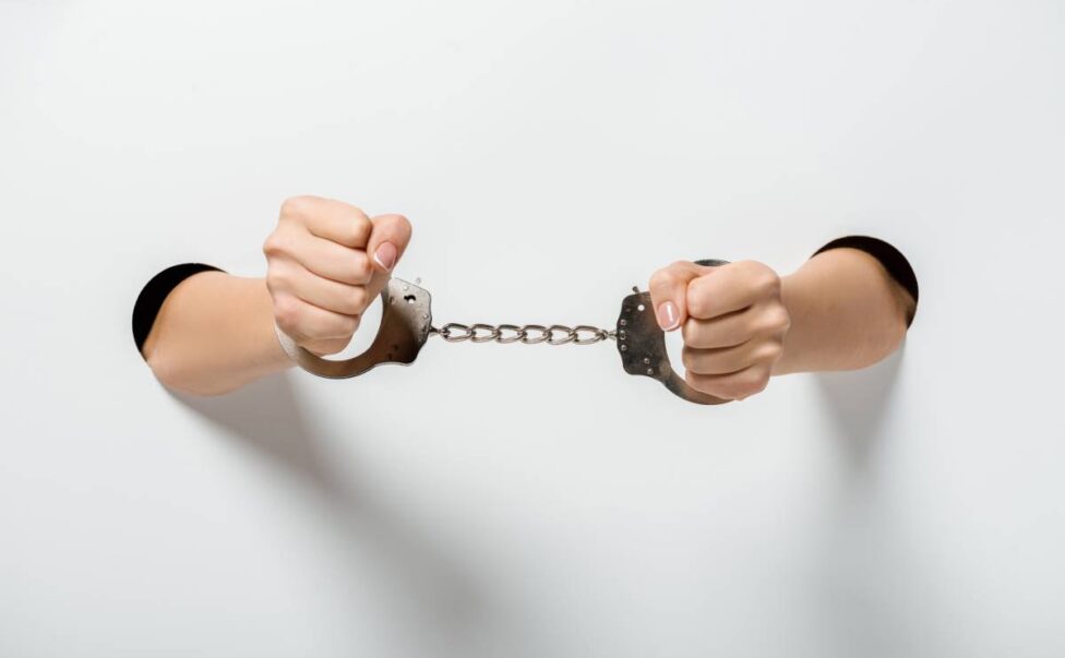 cropped image of girl in handcuffs holding hands through holes on white