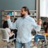 Handsome, confident businessman dancing in front of his team in modern office