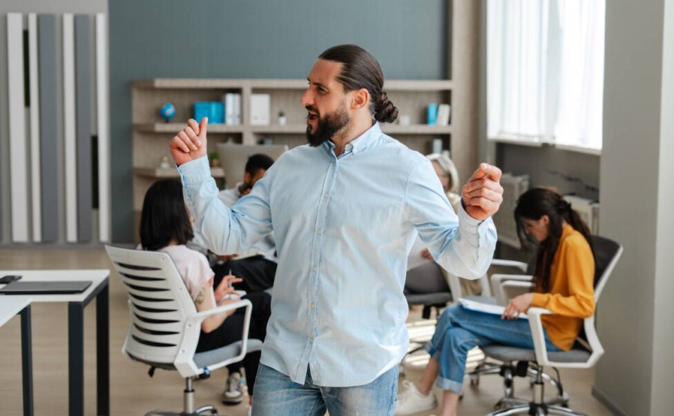 Handsome, confident businessman dancing in front of his team in modern office