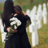 Embracing each other and crying. Two young women in black clothes visiting cemetery with many white crosses. Conception of funeral and Close Friend death
